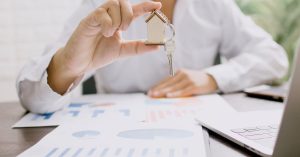 Real estate professional presenting a house model with keys, symbolizing property investment and ownership.